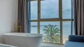 Un baño moderno con bañera, un ventanal con vistas al mar y un sofá azul.
