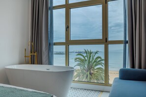 A modern bathroom with a bathtub, a large window with a view of the sea, and a blue sofa.