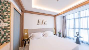 Habitación de hotel con una cama grande, una mesita de noche, una obra de arte colgada en la pared y una ventana con cortinas.