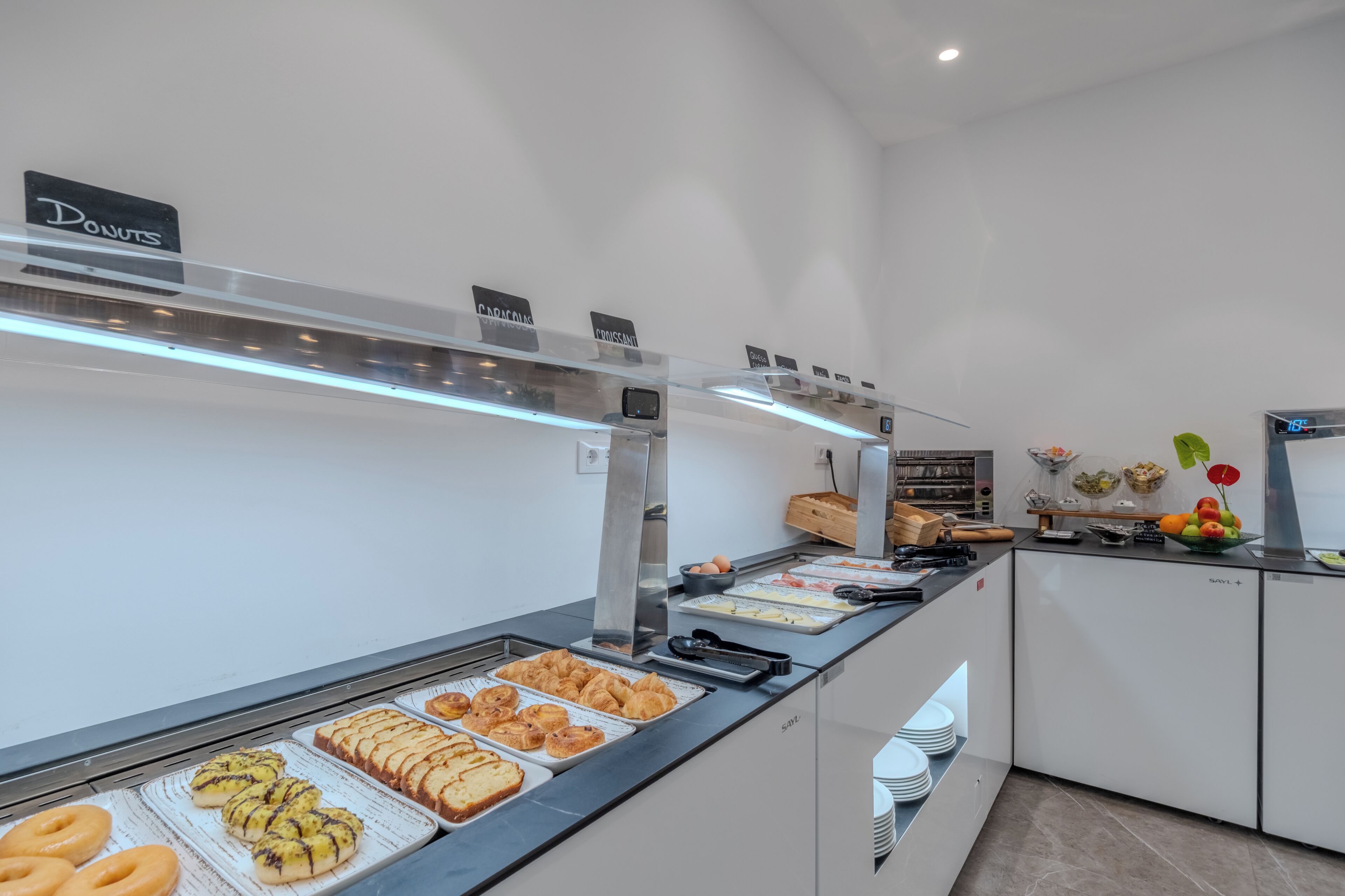 A buffet area with various food options, including donuts and pastries, and a refrigerator with fruits and vegetables.