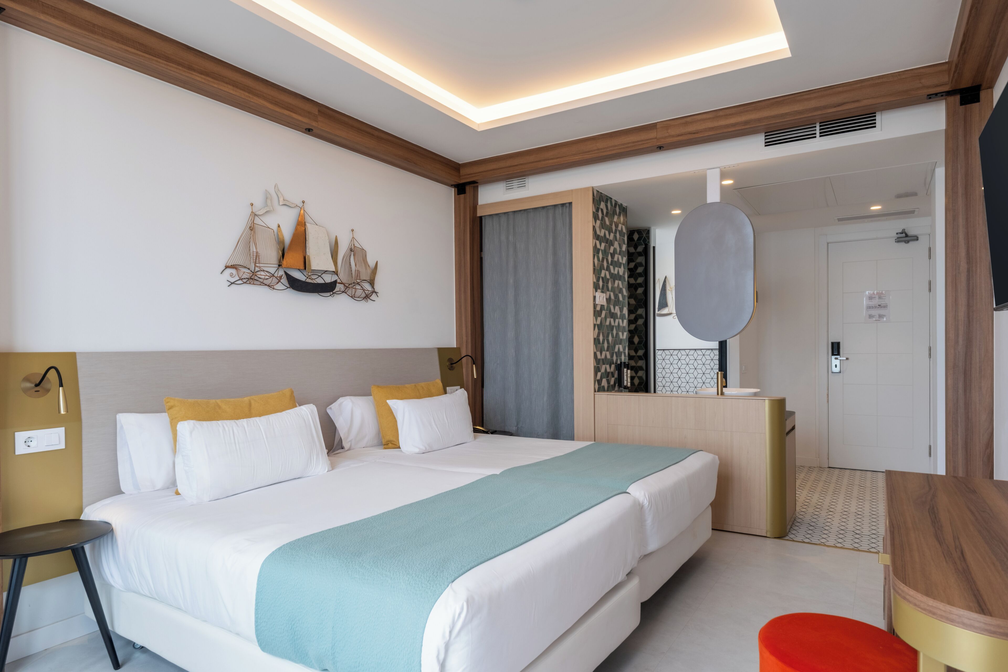 A modern hotel room with a large bed, a desk, a chair, and a bathroom visible through an open door.