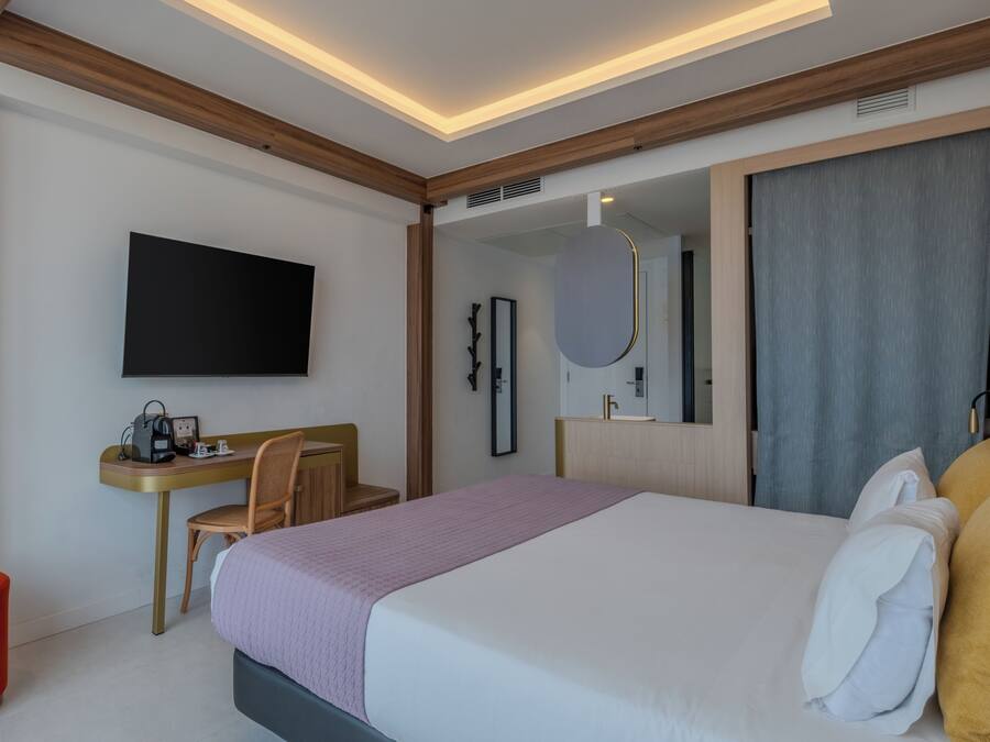 Ein modernes Hotelzimmer mit Bett, Schreibtisch, Sessel, Fernseher und einem großen Spiegel.