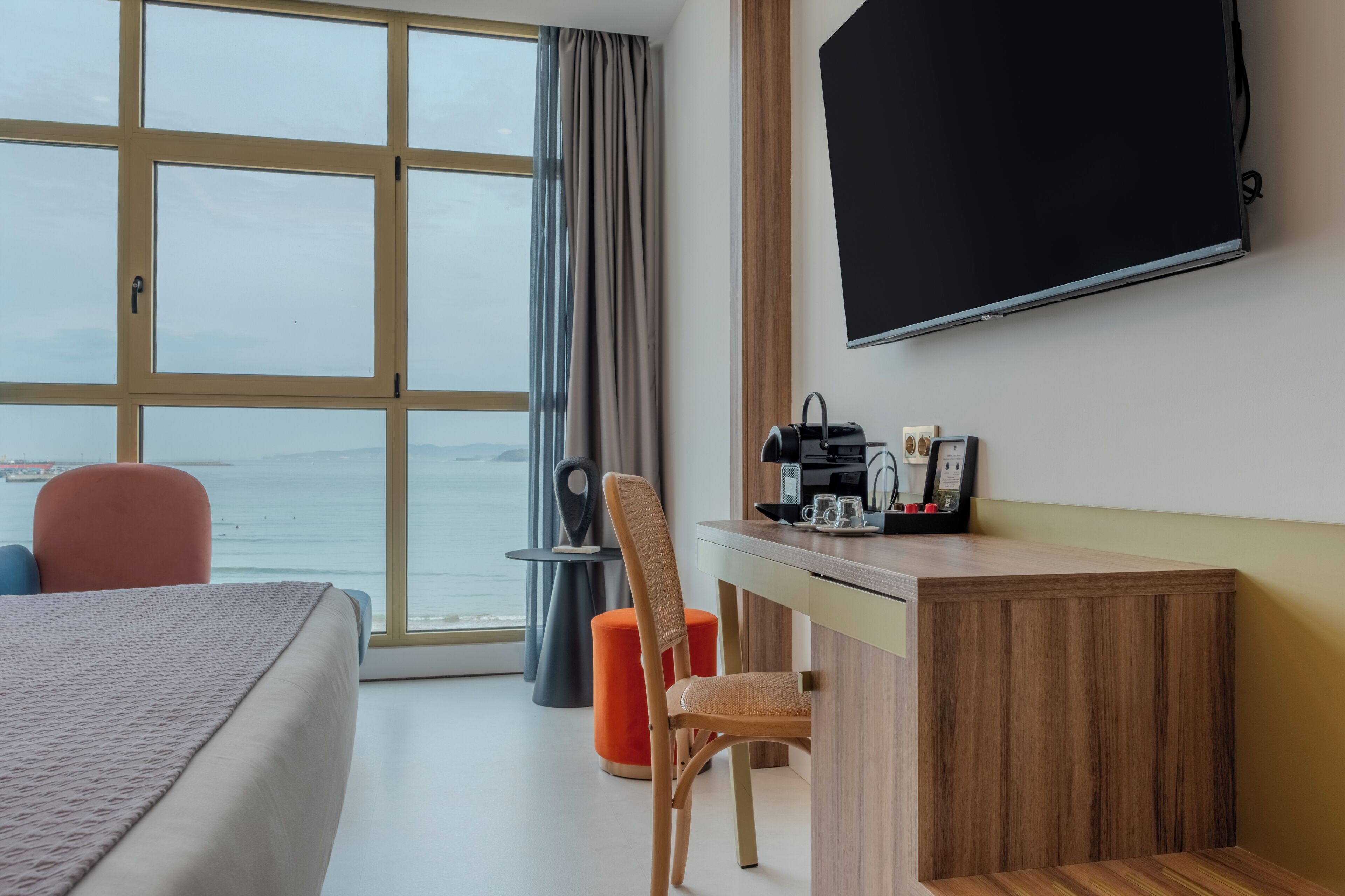 Habitación de hotel con cama, escritorio, silla, televisión y vista al mar.