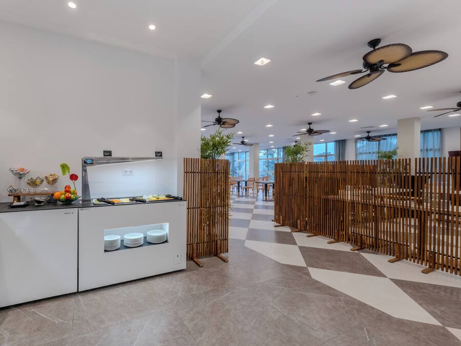 Un área de cocina moderna con mesas tipo bufé, ventiladores de techo y un piso con estampado de cuadros.