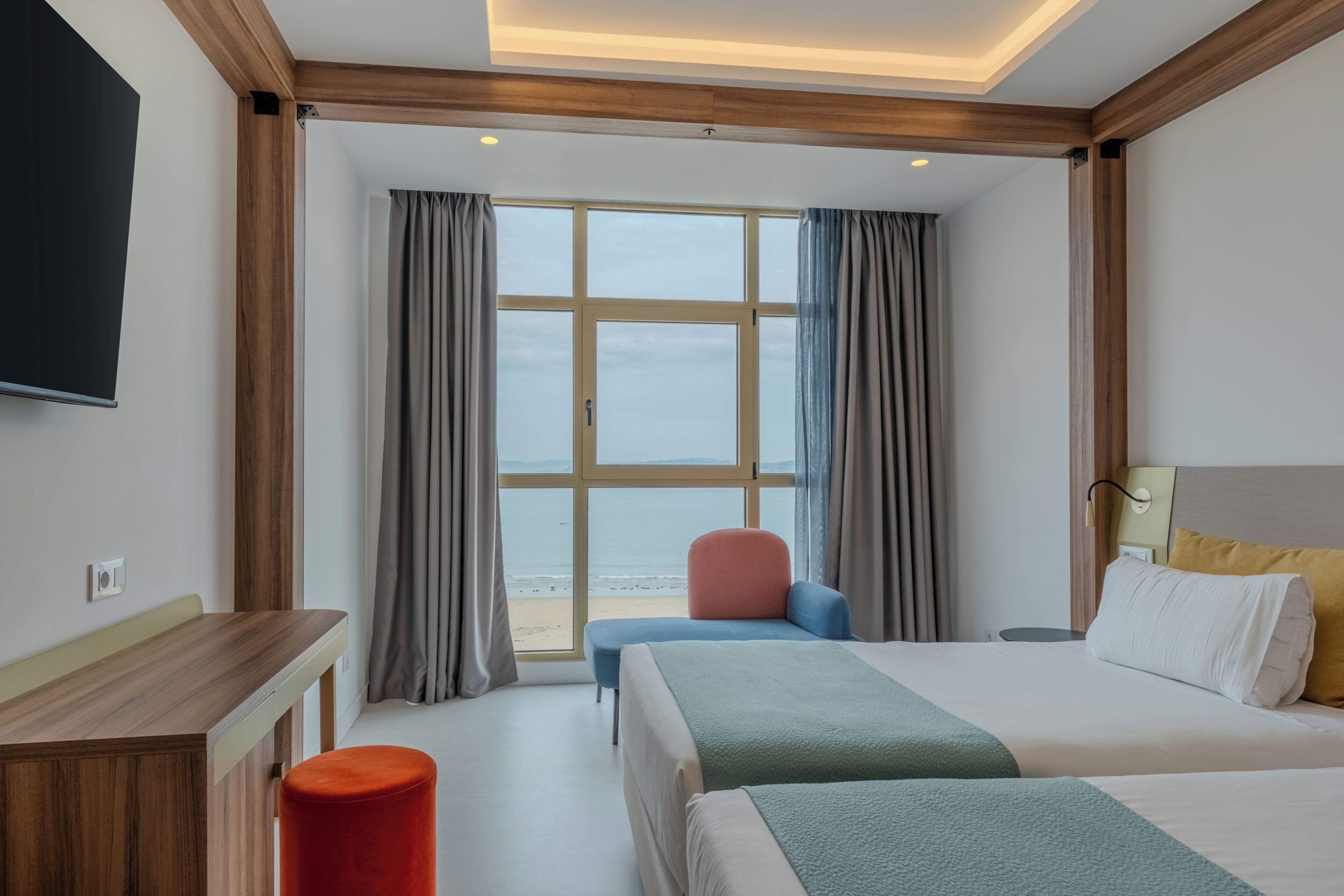 A hotel room with a large window, a bed, a desk, and a chair.