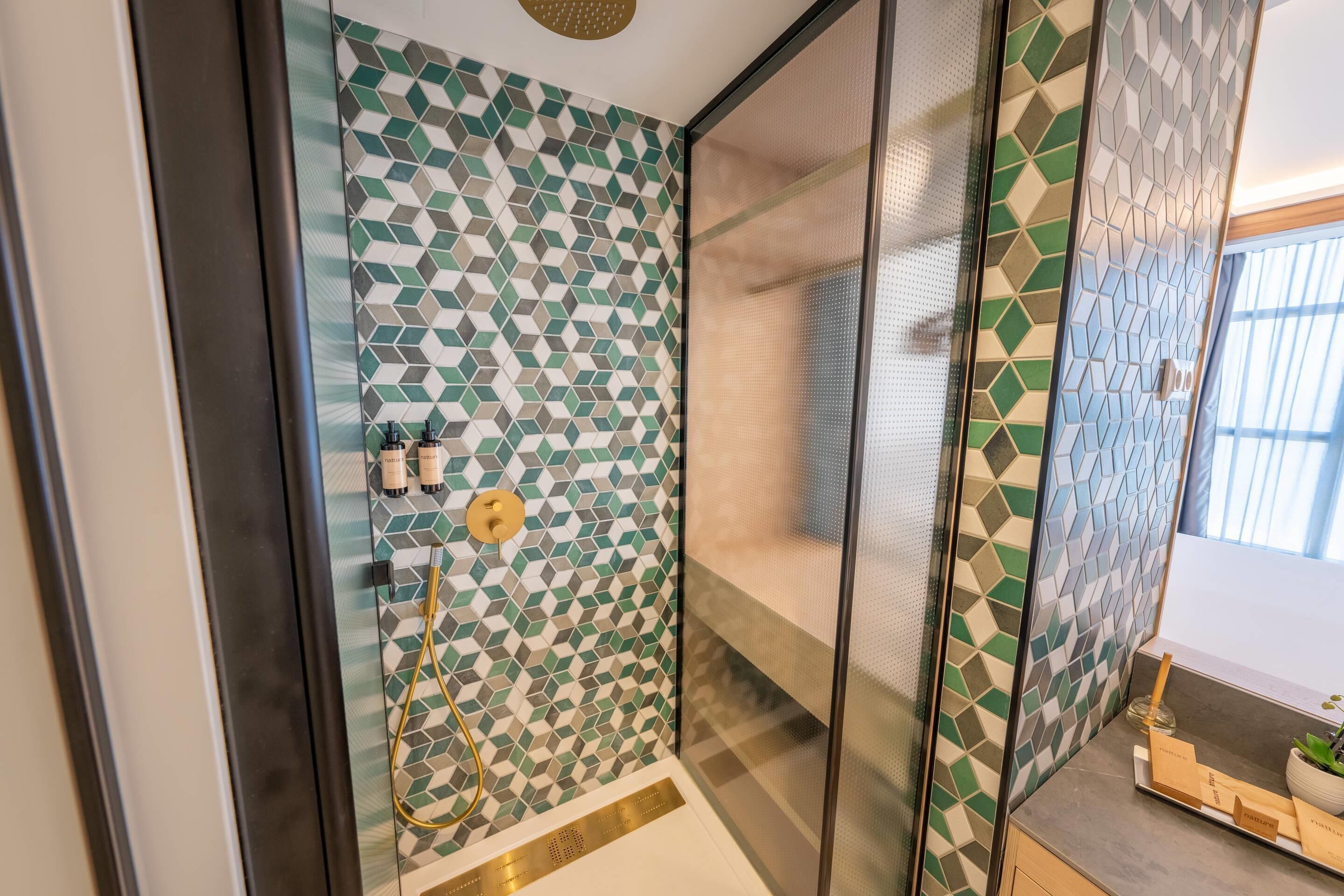 A shower with a geometric tile pattern, a gold showerhead, and a glass partition.
