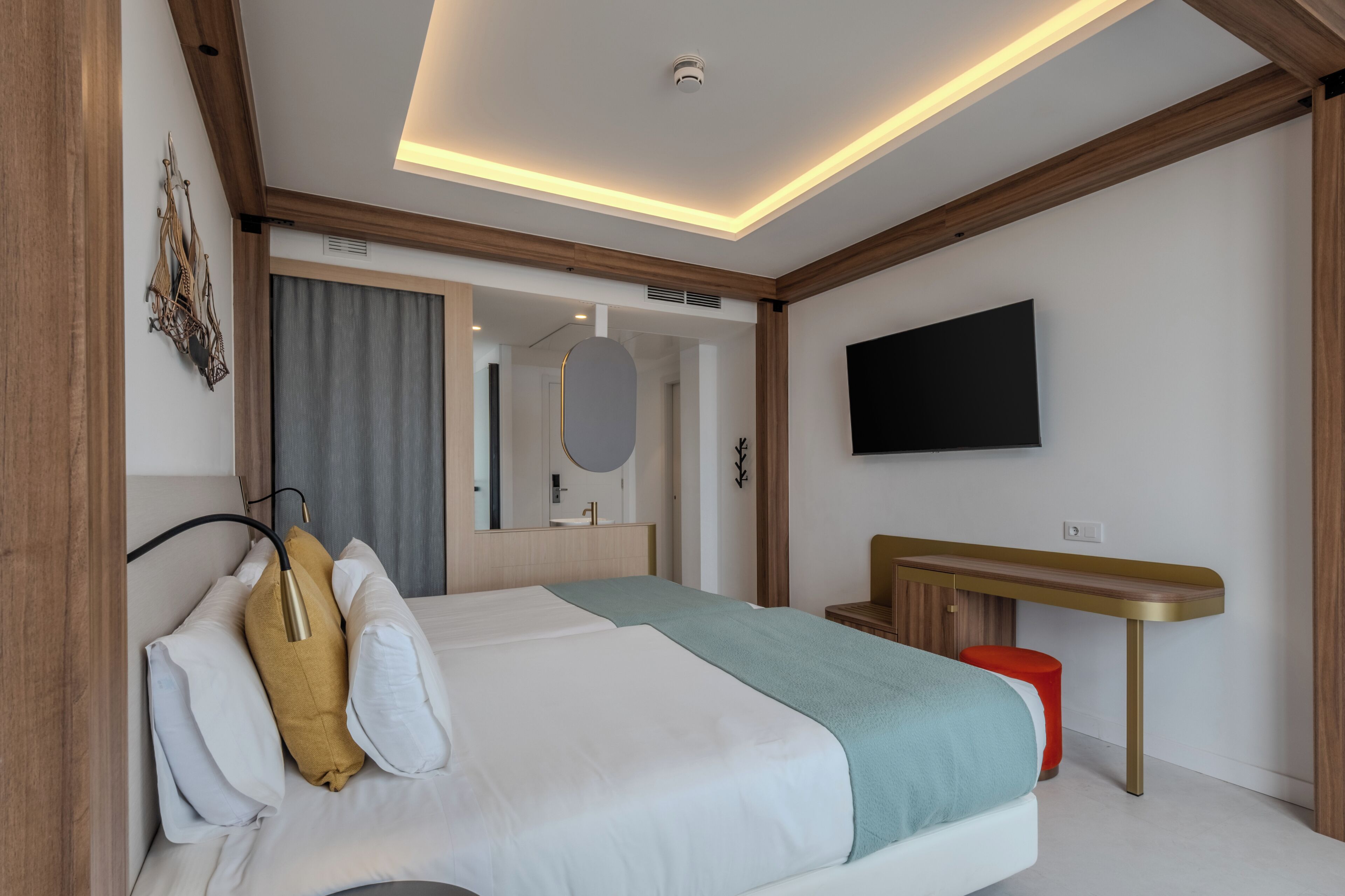 A modern hotel room with a bed, bedside table, TV, and a bathroom visible through an open door.