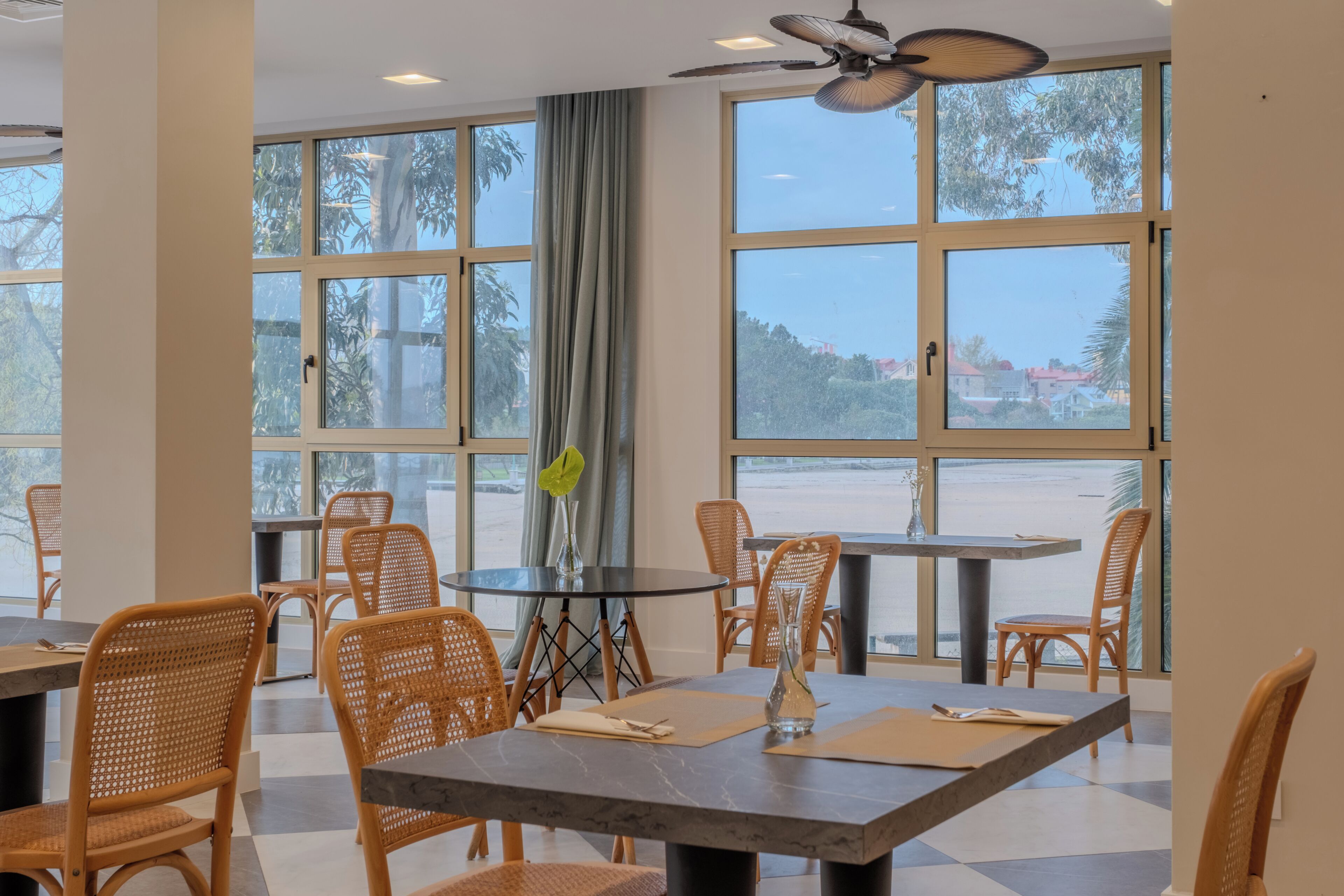 Uma área de refeições com cadeiras de vime, uma mesa redonda e grandes janelas com vista.