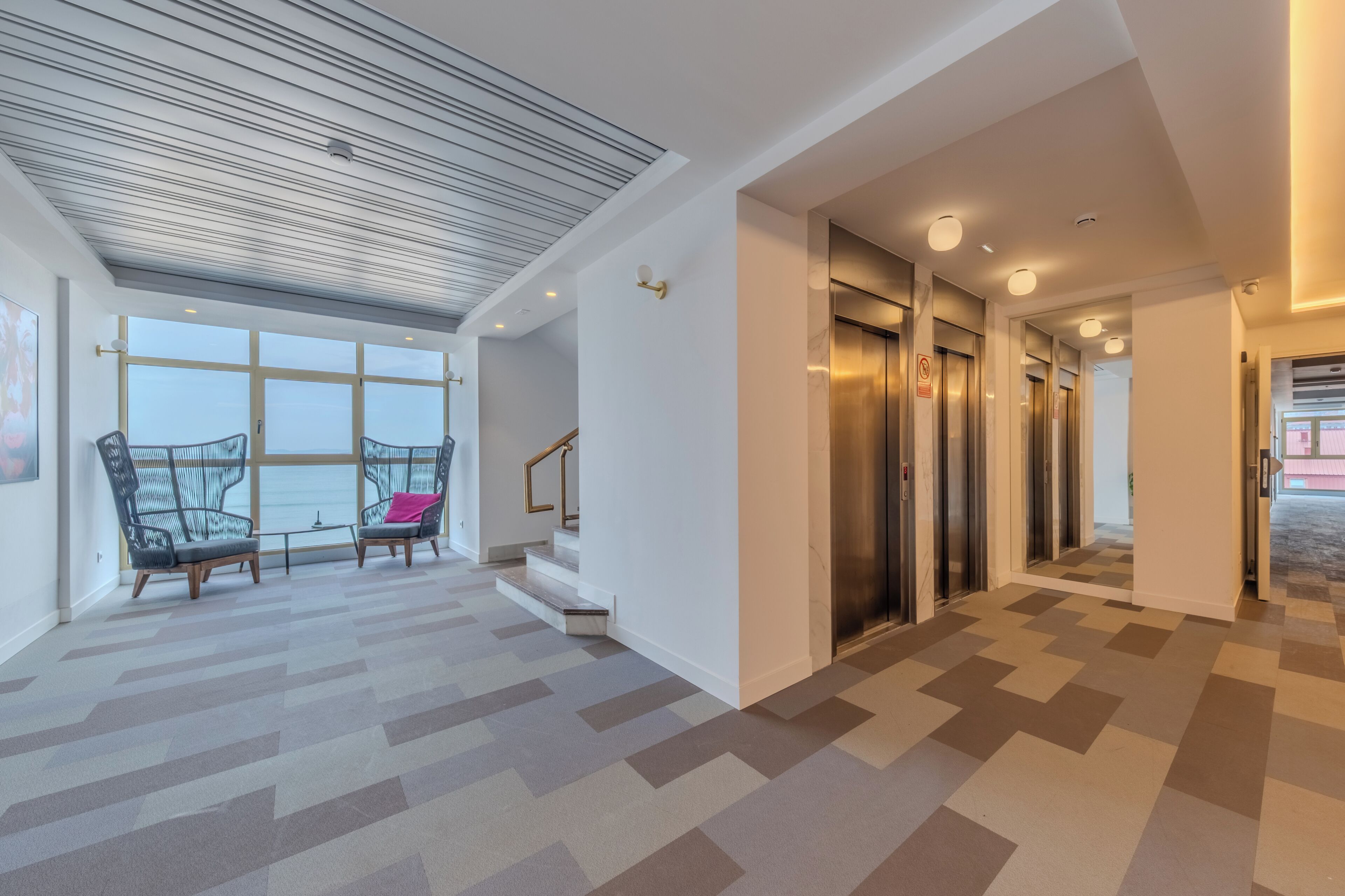 A modern interior with a checkered floor, two chairs, a staircase, and an elevator.