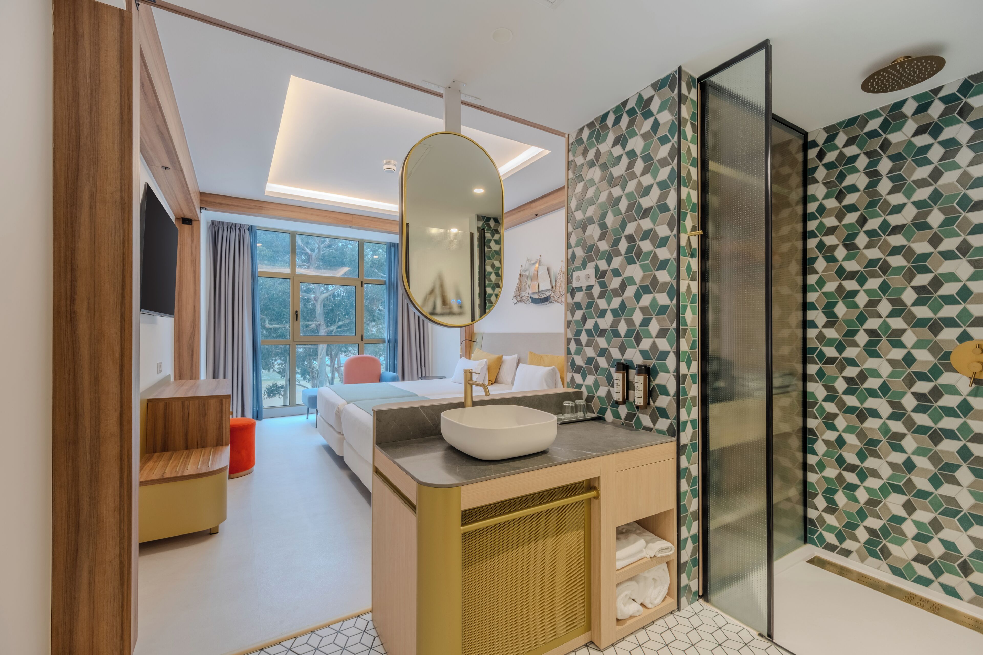 Habitación de hotel moderna con una cama grande, un baño con pared de azulejos geométricos, un espejo amplio y zona de ducha.