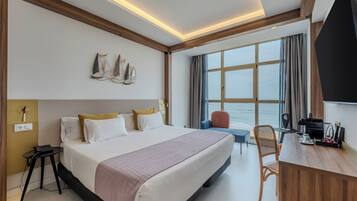 A hotel room with a large bed, a desk, a chair, a phone, and a window with curtains.