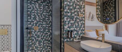 A modern bathroom with a geometric tile pattern, a glass-enclosed shower, a white sink, and a large mirror.
