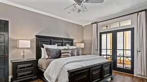 A bedroom with a dark wood bed, two bedside tables with lamps, a chandelier, and a view through a large window. - Wasser Haus | 4/3 with Private Pool and Hot Tub | Walk to Main (Fredericksburg)