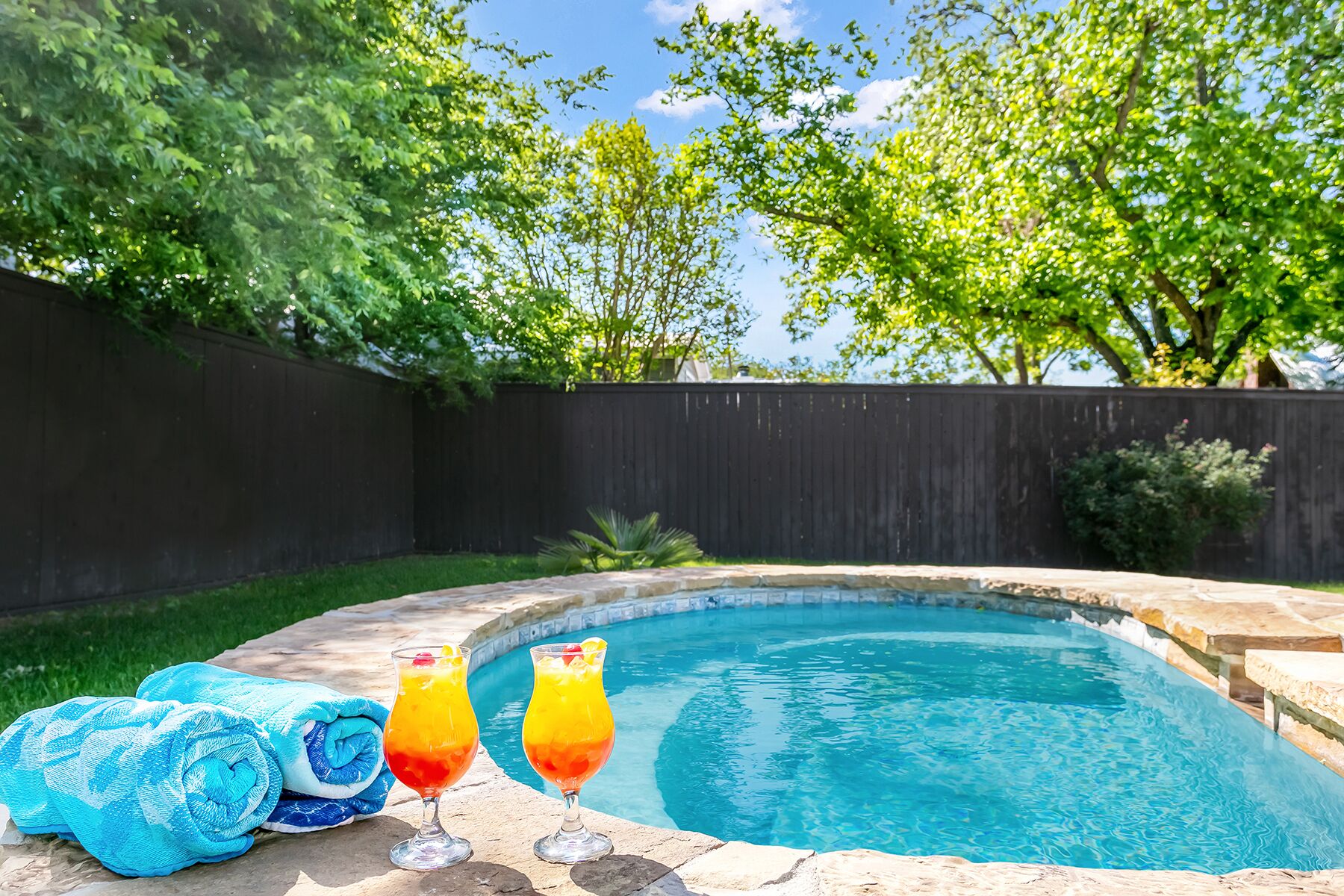 A backyard with a swimming pool, a wooden fence, and trees.