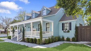 A light blue two-story house with a covered porch and a small front yard. - Wasser Haus | 4/3 with Private Pool and Hot Tub | Walk to Main (Fredericksburg)