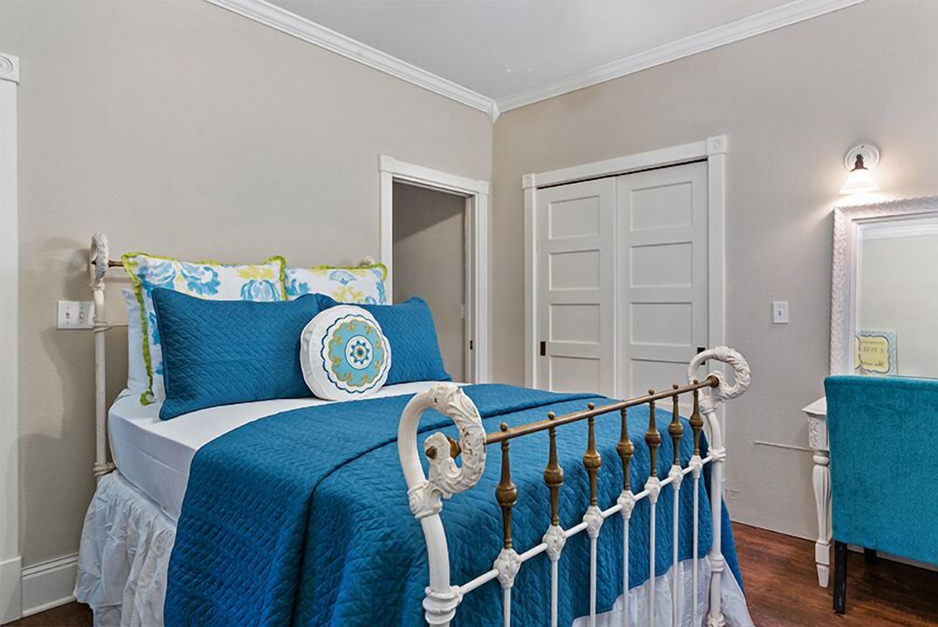 Un dormitorio con cama, paredes blancas, una puerta y una mesita con una silla.