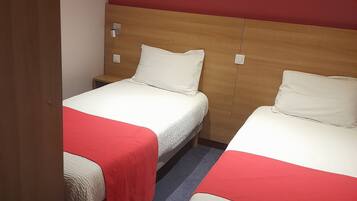 A hotel room with two beds, each with a white mattress and red bedspread.
