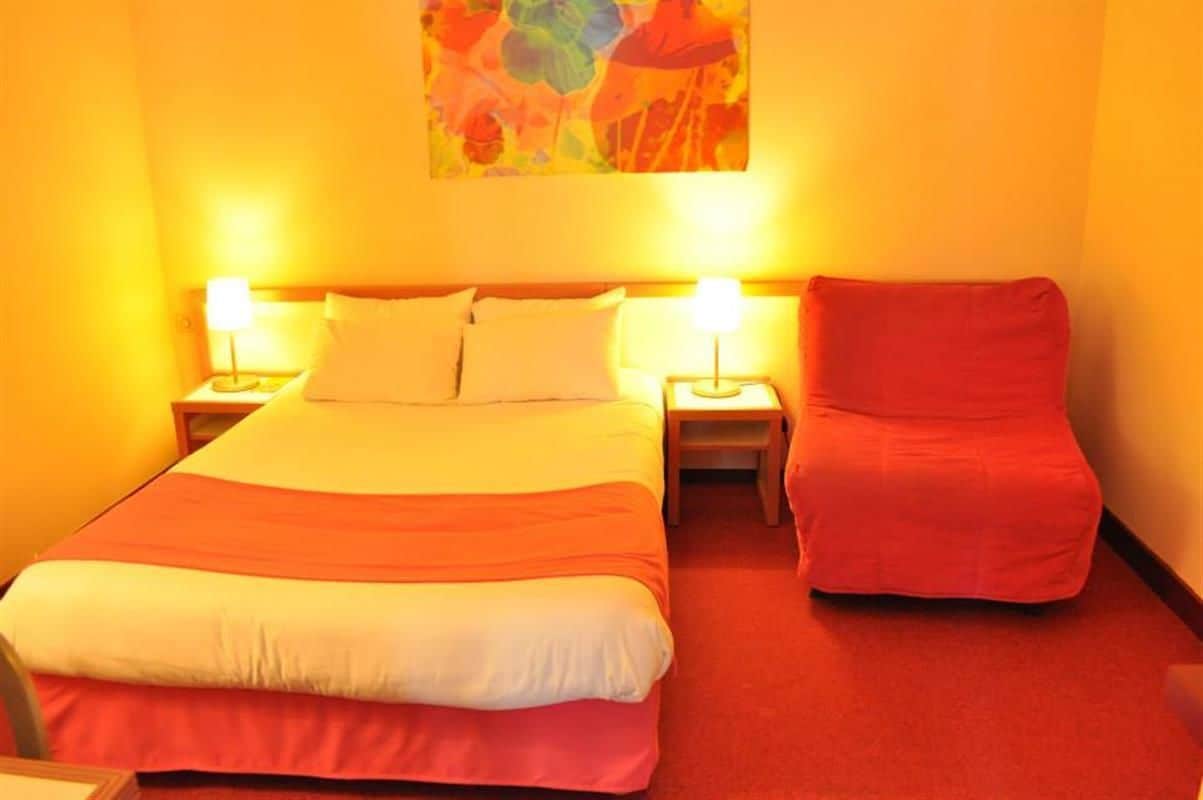 Habitación de hotel con una cama grande, dos lámparas de noche, una silla roja y un cuadro abstracto colorido en la pared.