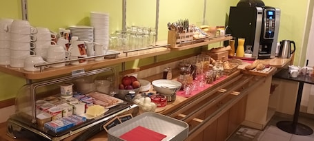 A breakfast buffet with various food items, utensils, and a coffee machine.