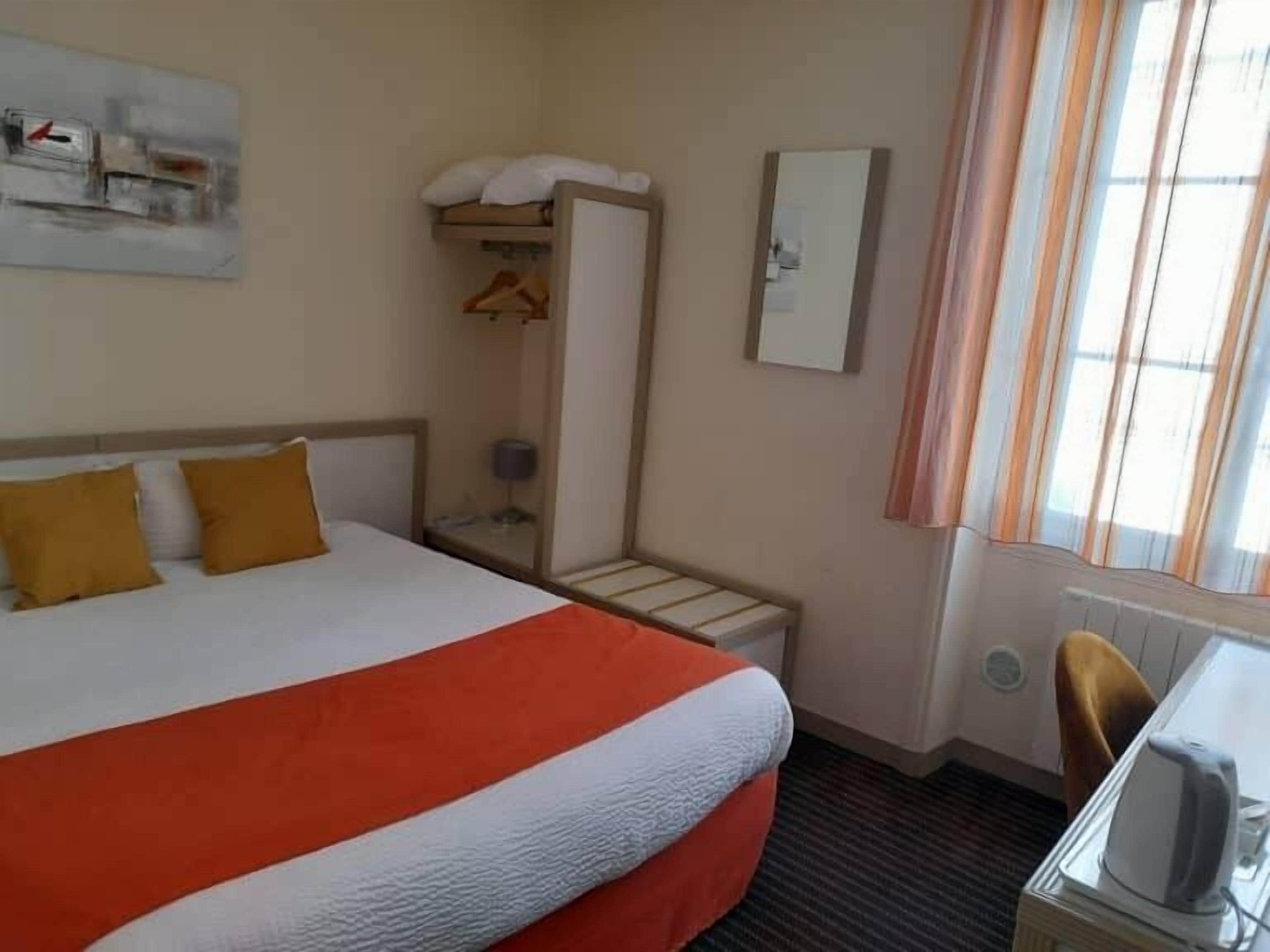 A hotel room with a large bed, a desk with a kettle, and a window with curtains.