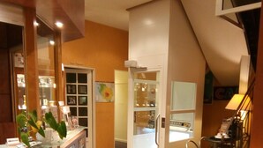 Eine Hotelhalle mit einer Rezeption, einer Glastheke, einer Sitzecke mit Stühlen und einer Treppe zu einer oberen Etage.