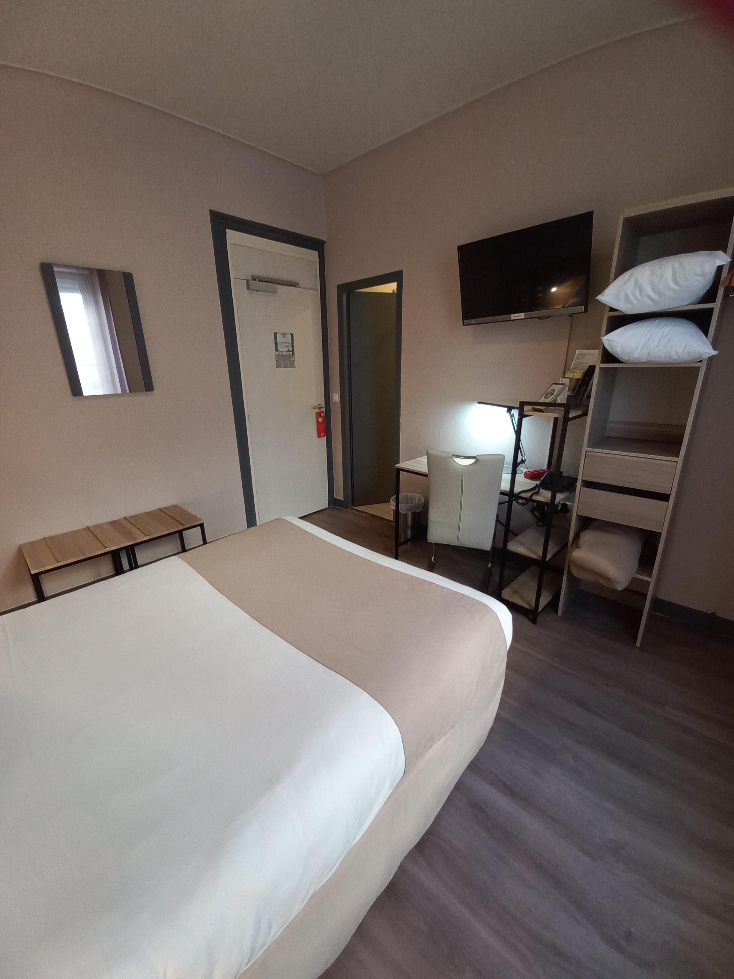 A hotel room with a large bed, a desk with a chair, a TV mounted on the wall, and a bunk bed with pillows.