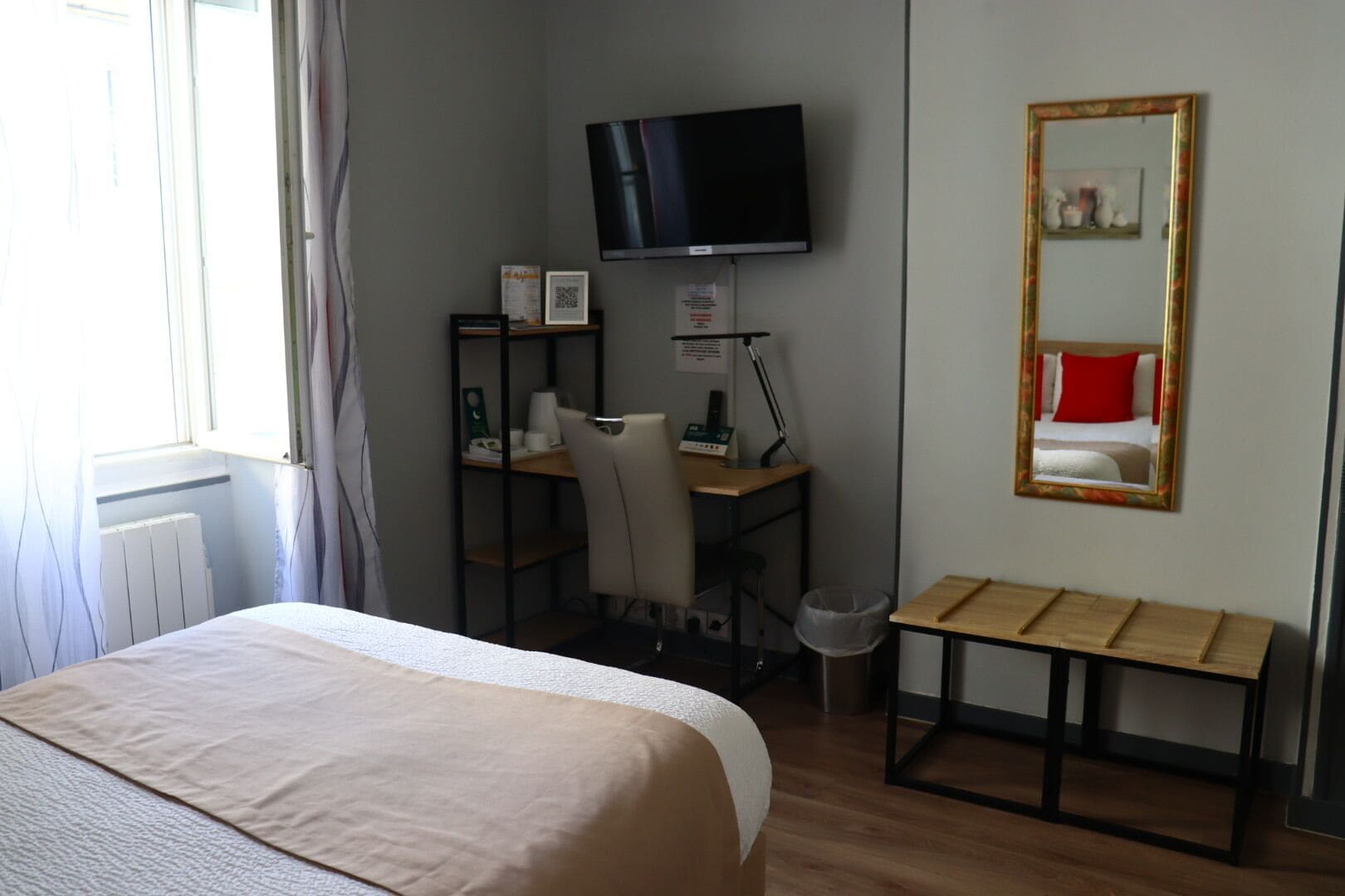 Une chambre d’hôtel comprenant un lit, un bureau avec une chaise, une télévision, un miroir et une petite table.
