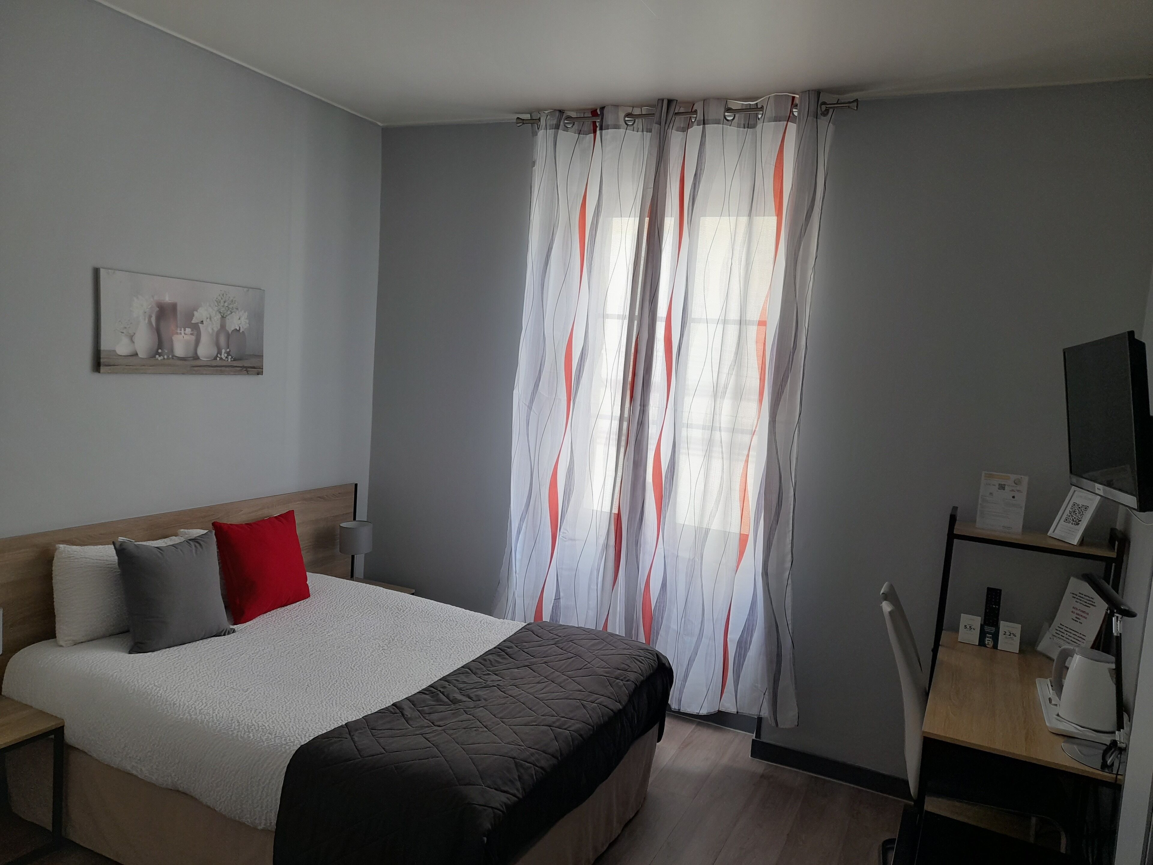 Habitación de hotel con cama, escritorio, silla, televisor y ventana con cortinas.