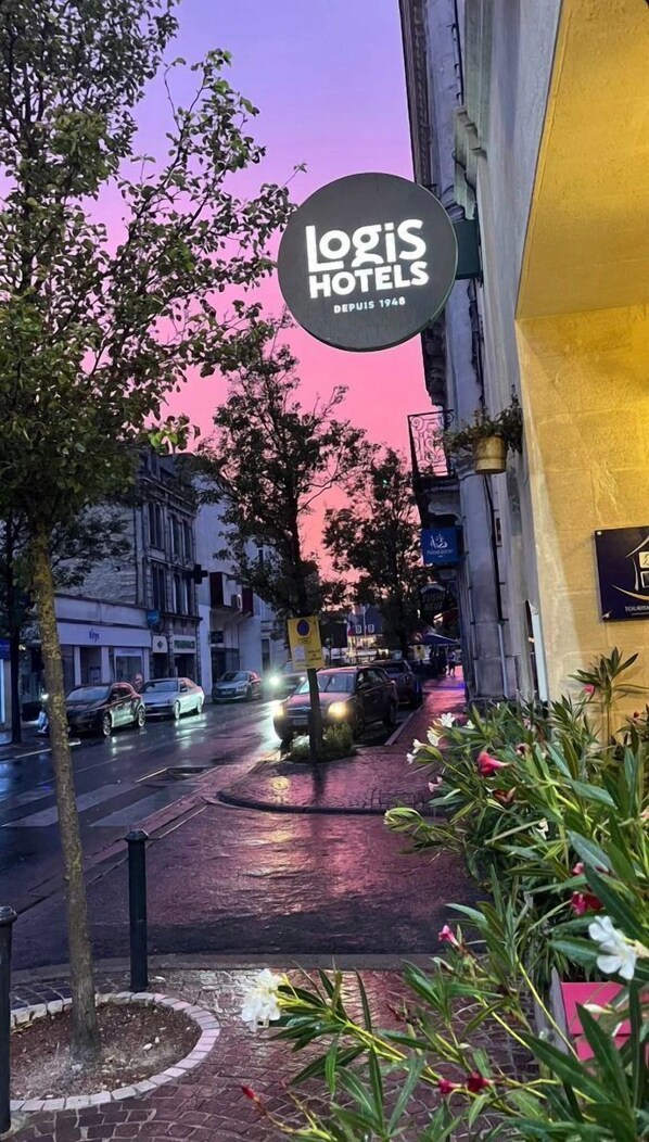 Udsigt over en gade med en bygning med teksten "Logis Hotels" og en lyserød himmel i baggrunden.