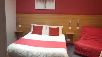A hotel room with a large bed, a red chair, a wooden headboard, and a colorful abstract painting on the wall.