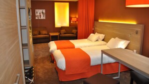 Ein Hotelzimmer mit zwei Betten, einem Schreibtisch, einem Sessel, einer Couch und einer Lampe.