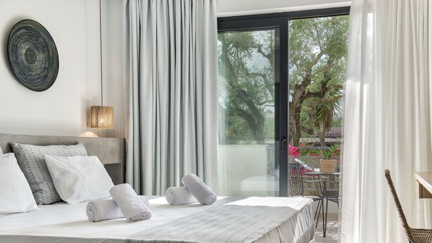 Een moderne hotelkamer met een groot bed, uitzicht op de omgeving en een balkon met een tafel en stoelen.