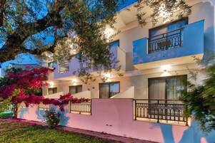 Un edificio de varios pisos con balcones, un jardín con plantas florecientes y una fachada bien iluminada.
