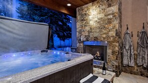 A hot tub with a stone wall and a fireplace, wooden ceiling, and outdoor seating area.