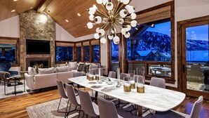 A modern living room with a large stone fireplace, a television, and a dining area with a marble table and chairs.