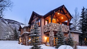 A large, multi-story lodge with a stone facade, a balcony, and a snow-covered landscape.