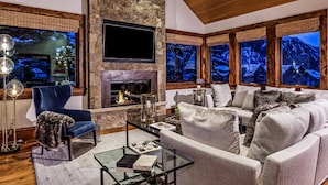 A cozy living room with a stone fireplace, comfortable seating, and large windows with a snowy mountain view.