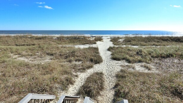 A beach path leading to the ocean with a clear sky.