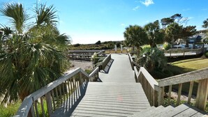 A wooden boardwalk leading to a beach area with palm trees and a clear blue sky.