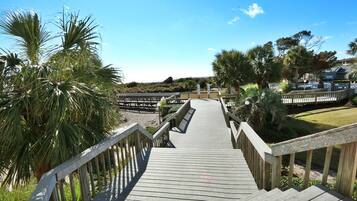 A wooden boardwalk leading to a beach area with palm trees and a clear blue sky.