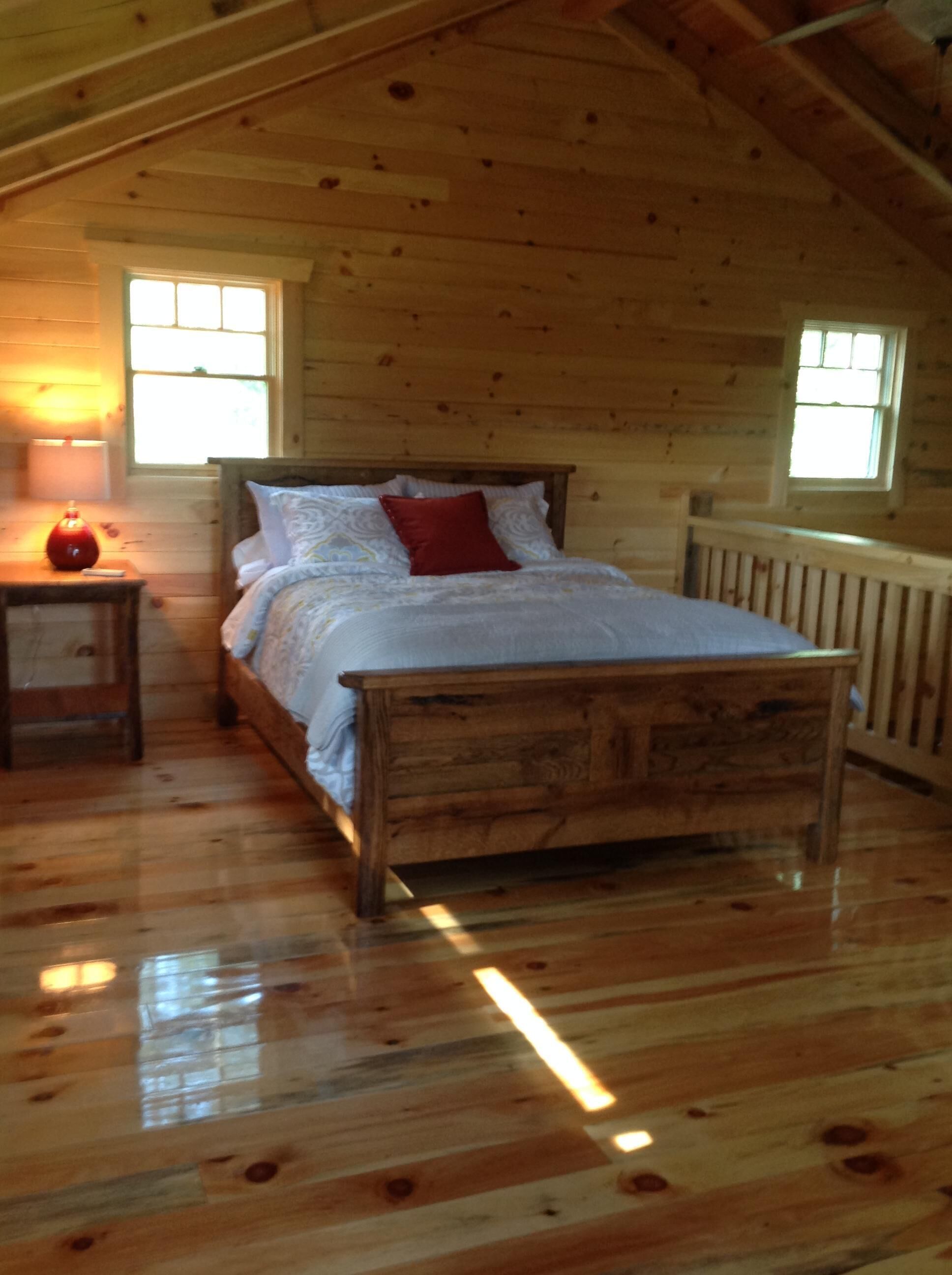 A wooden cabin bedroom with a bed, a nightstand, and two windows.