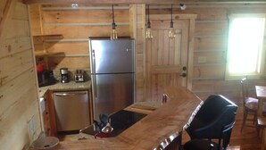 A compact kitchen with wooden walls, a stainless steel refrigerator, a coffee maker, and a sink.