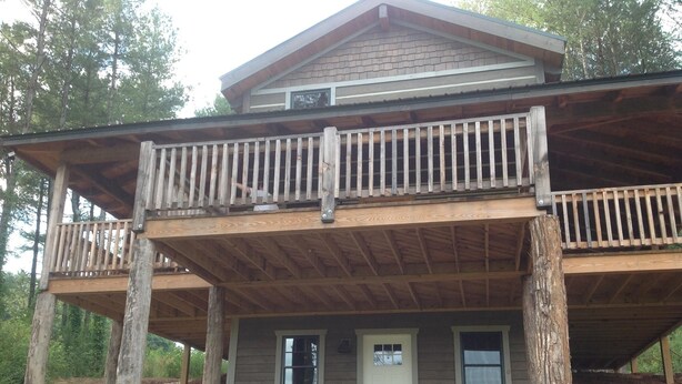 A two-story wooden cabin with a balcony, stone foundation, and a front door.