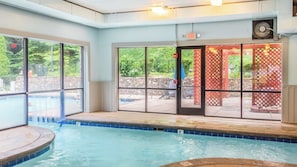Ein Innenpool mit großen Glaswänden, eine Whirlwanne und eine Terrasse mit Sitzmöglichkeiten im Freien.