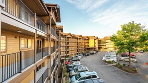 Un hotel de varios pisos con balcones, estacionamiento y un árbol.