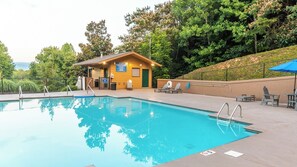 Una piscina con un edificio de madera al fondo, rodeada de árboles.