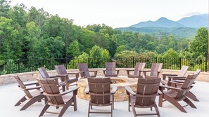 Un espace de détente circulaire, avec des chaises disposées autour d’un foyer central, le tout agrémenté d’une végétation luxuriante et offrant une vue sur des montagnes lointaines.