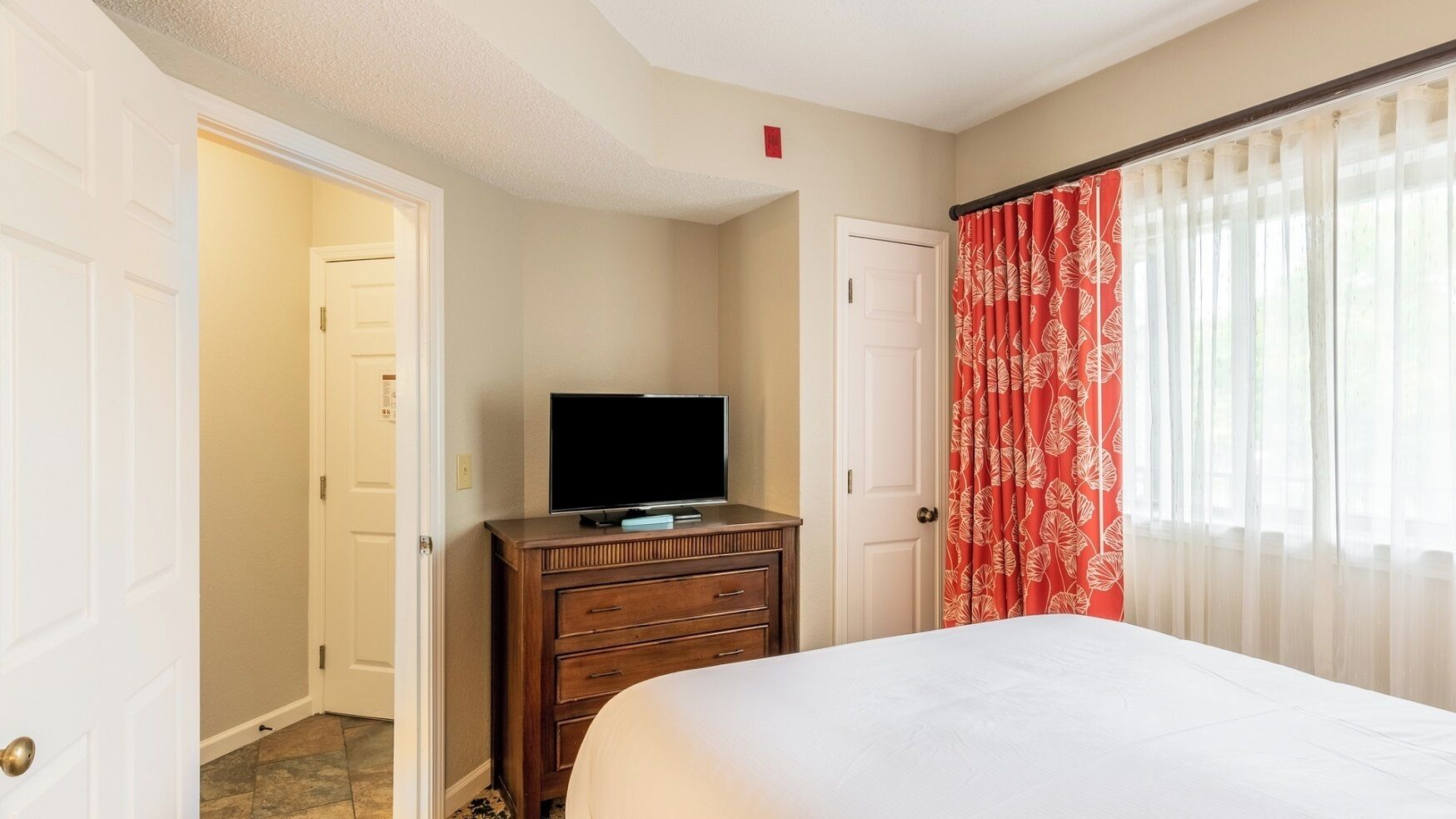 Quarto de hotel com uma cama, cômoda, televisão e porta que dá para outro quarto.