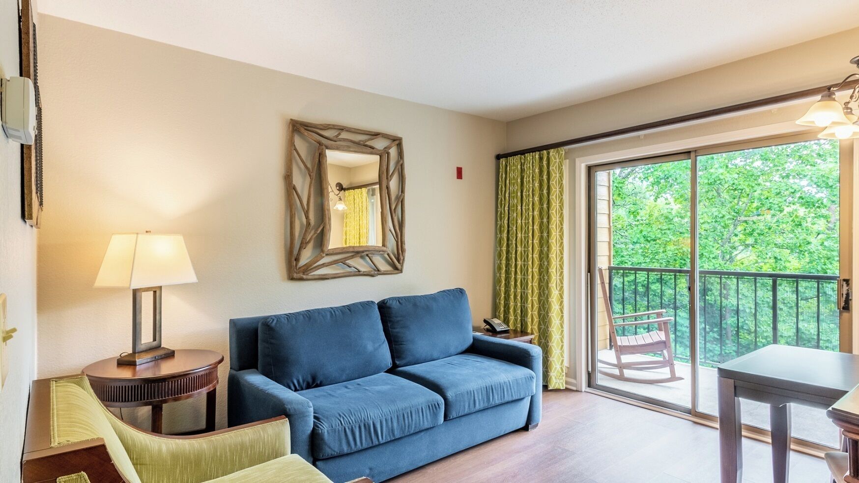 Un salon comprenant un canapé, une lampe, un miroir, un balcon avec une chaise et une table.