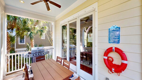 A covered outdoor area with a grill, a table, chairs, a lifebuoy, and a pool rules sign. - Beautiful 6 bedroom home with private pool 2 blocks from beach (Isle of Palms)